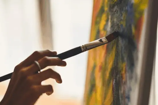 Close up photo of a hand holding a brush, painting a canvas