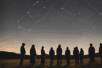 People standing in a field looking up at a constellation.