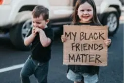 A young girl holds a sign that reads "My Black Friends Matter"