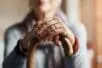 An older woman rests her hands on a cane