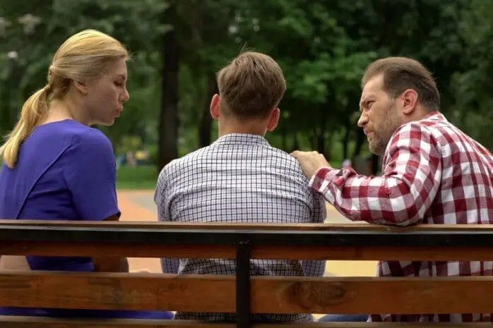 Two parents sit on a bench with their teen