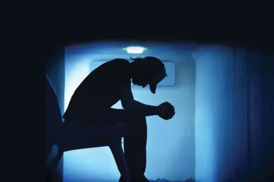 A teenager looks at the floor with his elbows on his knees