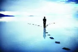 A figure walking on a path of stones through water and reaches as fork