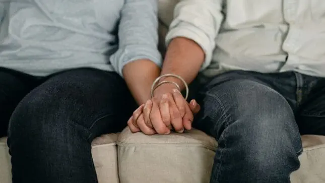 Two people holding hands on a couch | Photo by Ketut Subiyanto/Pexels