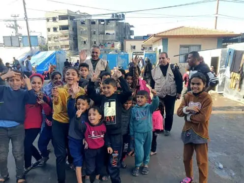 A group of Gazan children waving with adults in the background