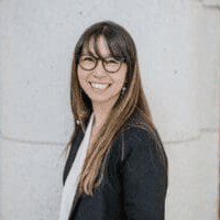 Woman with glasses by white wall smiling
