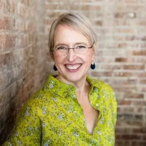 Woman in green shirt against brick backdrop smiling