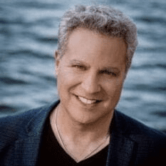 Grey-haired man smiling in front of water in a blazer