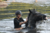 A woman sits joyfully on a horse emerging from water