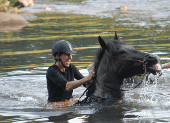 A woman sits joyfully on a horse emerging from water