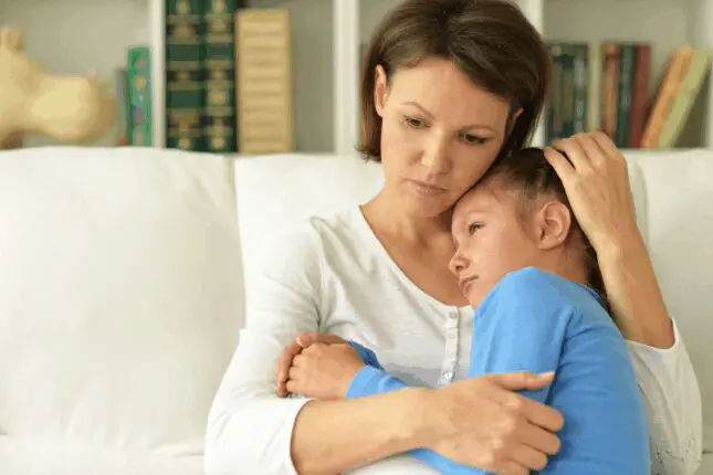 Image of a mother holding her upset daughter as they sit on a couch