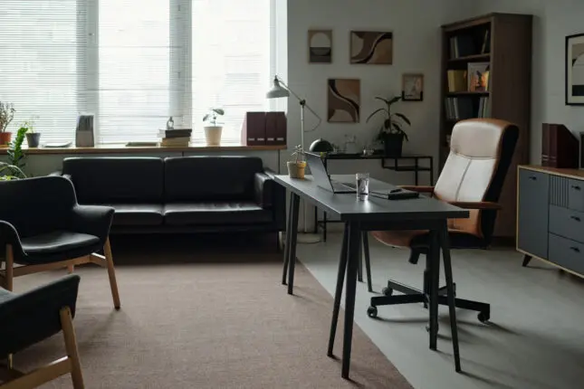 An empty therapist office with a desk, two chairs, and a couch