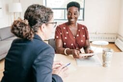 Two women sitting at a table with papers talking and smiling