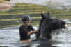 A woman sits joyfully on a horse emerging from water