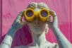 A statue stares through a pair of bright yellow binoculars