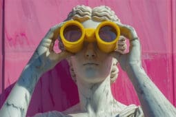A statue stares through a pair of bright yellow binoculars