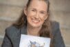 Megan Connell holding a D&D book and smiling to camera