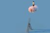 A figure stands atop a pink cloud, having left a tall ladder behind